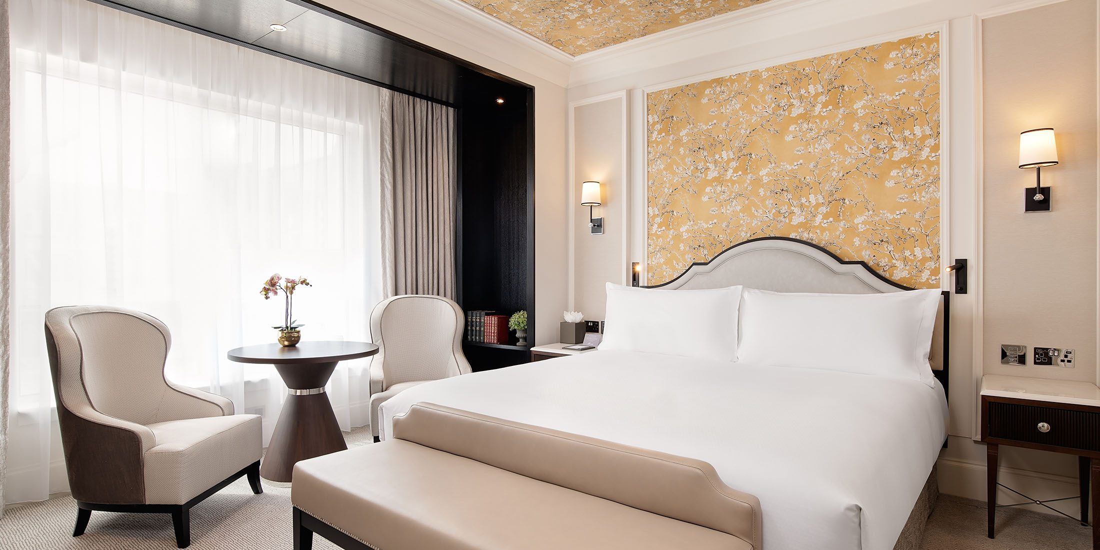 King room at Fairmont Windsor Park with a king-sized bed, floral wallpaper, and a cosy seating area by a large window.